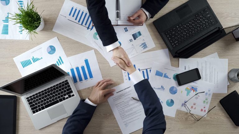 Business professionals shaking hands over documents and graphs